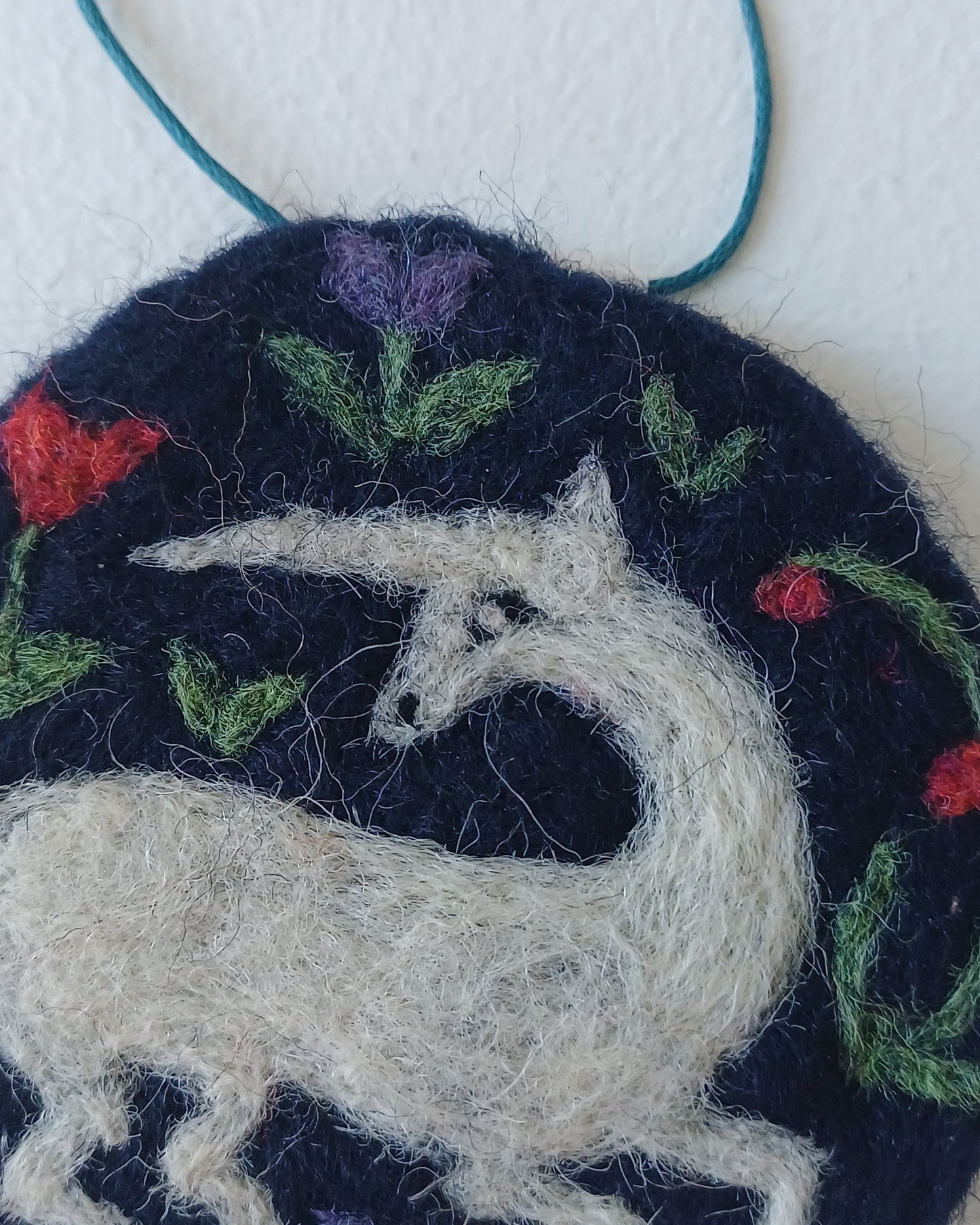 needle felted decoration with a white unicorn design on a dark blue background