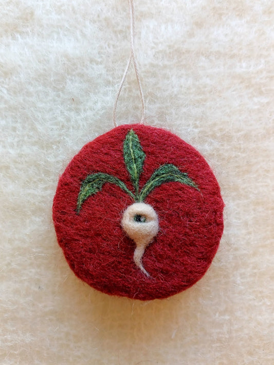 A red circular hanging decoration, needle felted with a 3D, white radish with one eye and 3 green leaves.