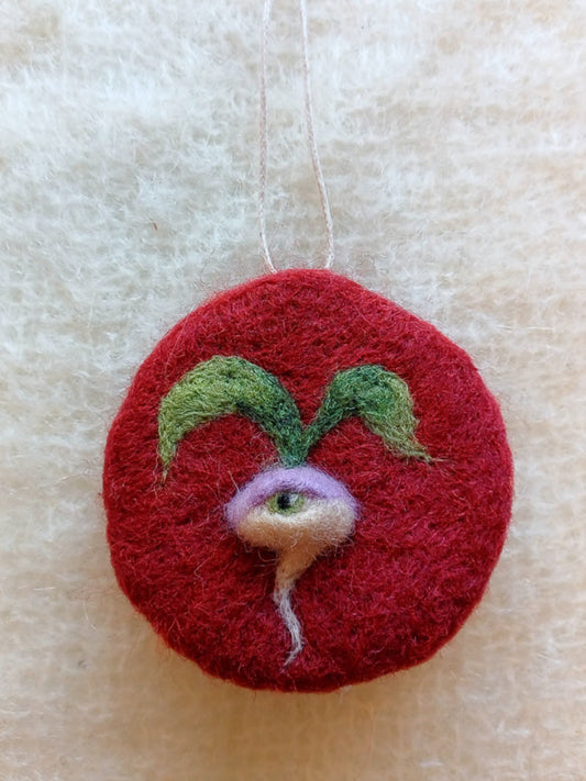 A red circular hanging decoration, needle felted with a one-eyed turnip. Inspired by medieval illustration.