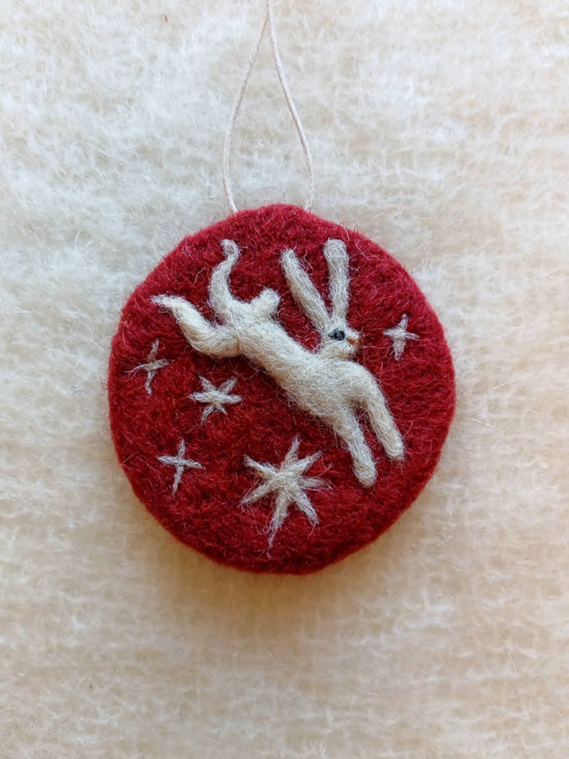 Red needle felt ornament with white needle felted hare design  leaping through stars on a beige knitted background
