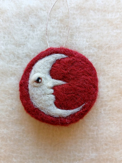 needle felted Red and white crescent moon ornament on a beige wool background