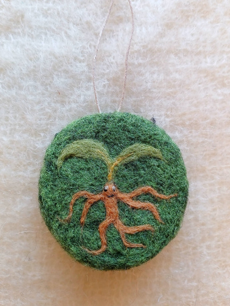 Green felt ornament with a plant design on a beige background - a mandrake plant inspired by medieval magic illustrations