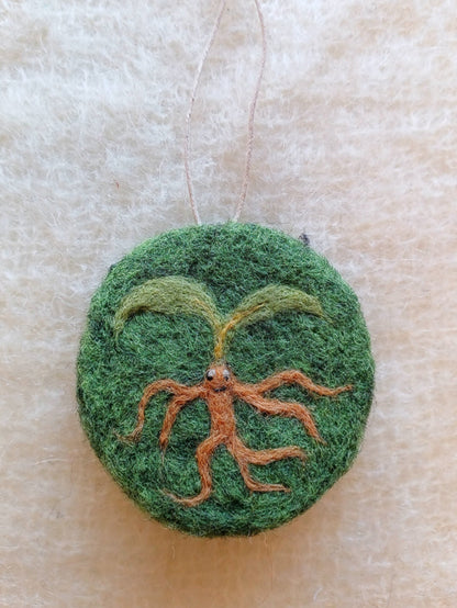 Green felt ornament with a plant design on a beige background - a mandrake plant inspired by medieval magic illustrations
