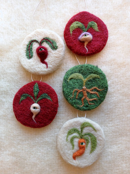 A collection of 5 needle felted circular decorations that feature medieval style vegetables, each with one eye. A mandrake, turnip, radish, carrot and beetroot, on white red or green backgrounds. 