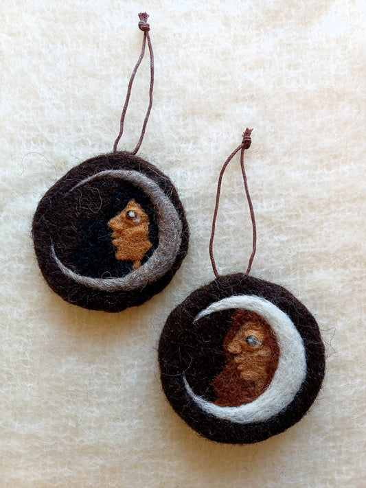 Two dark brown needle felted hanging ornaments, each colour variations of the same design; a crescent moon with a woman looking out.
