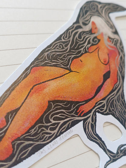 A die-cut sticker featuring a stylized illustration of a nude female figure with flowing dark hair, printed on a white backing and photographed on a light wood surface.