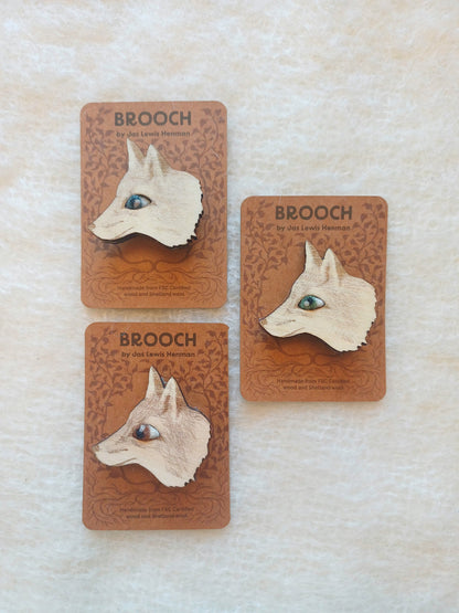 Three small brooches shaped like fox heads are displayed on brown backing cards on a light textured fabric background. The cards read BROOCH and show the brand as Jas Lewis Henman