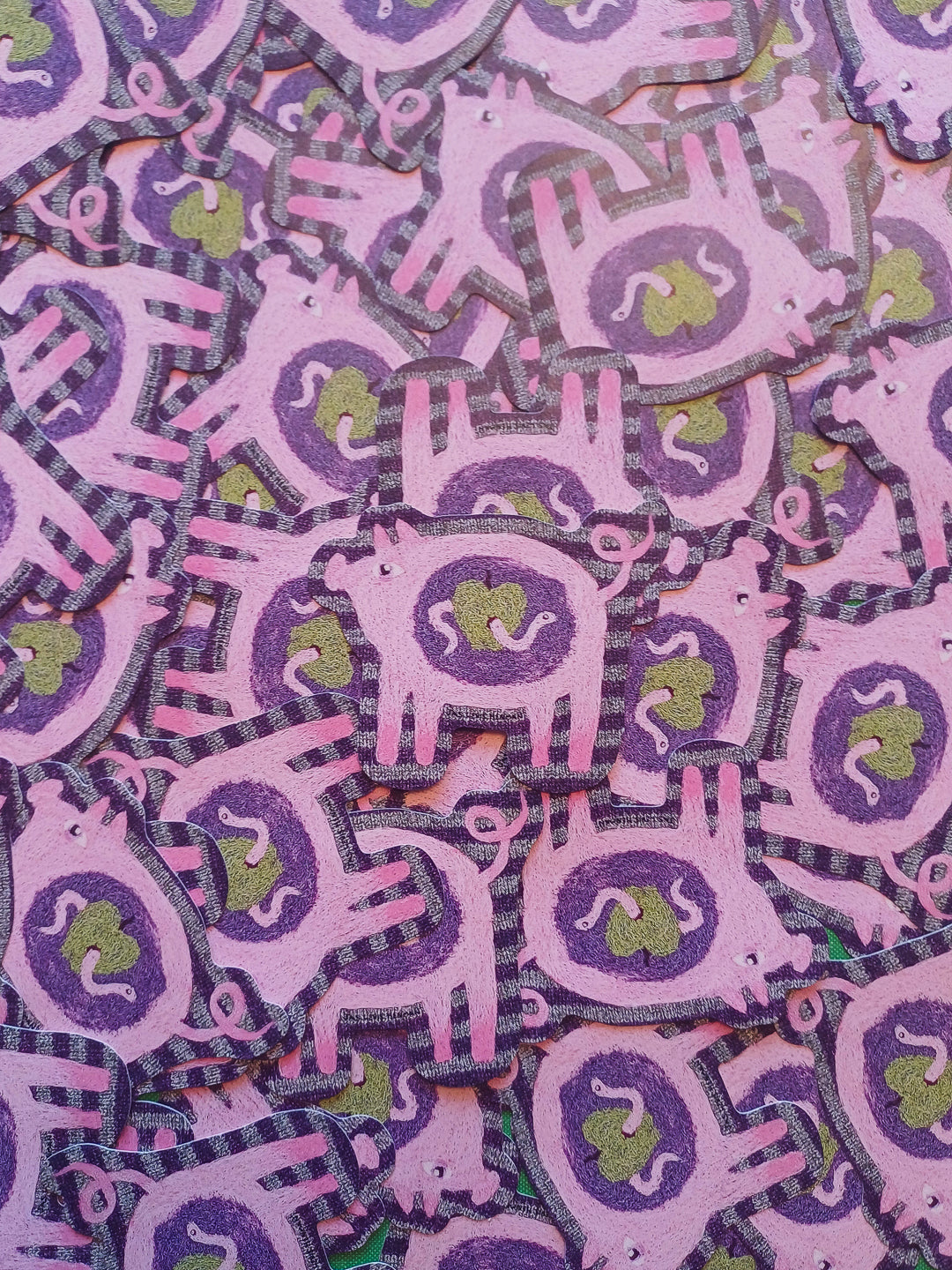 A close-up of many overlapping pink and purple pig-shaped stickers with green apple centers, filling the frame.