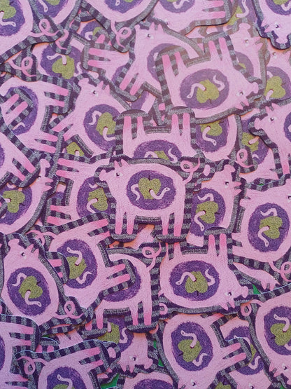 A close-up of many overlapping pink and purple pig-shaped stickers with green apple centers, filling the frame.